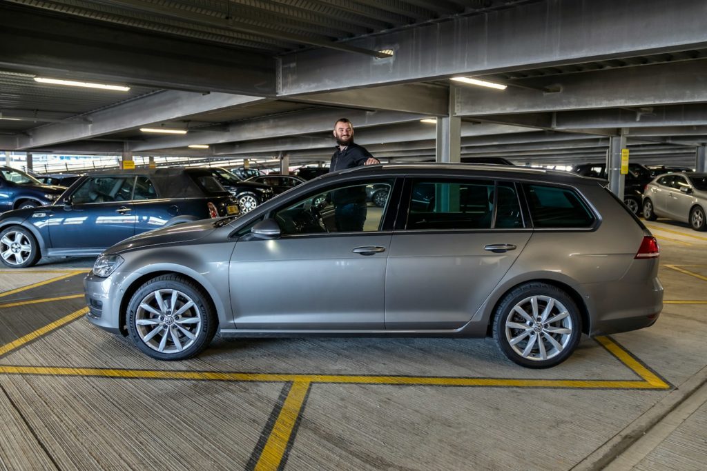 Man standing by a silver station wagon in parking garage